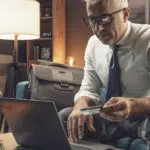 Confident businessman sitting on the couch at home and using his credit card online, he is doing online-banking